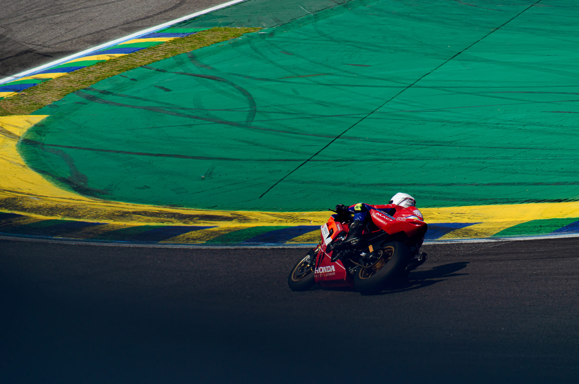 Honda vermelha #44 da Honda Repsol CB Racing, da classe GP1000, inclinada rente às zebras verde, amarela e azul com Gui Brito na Moto1000GP 2026 - Etapa 5, Interlagos