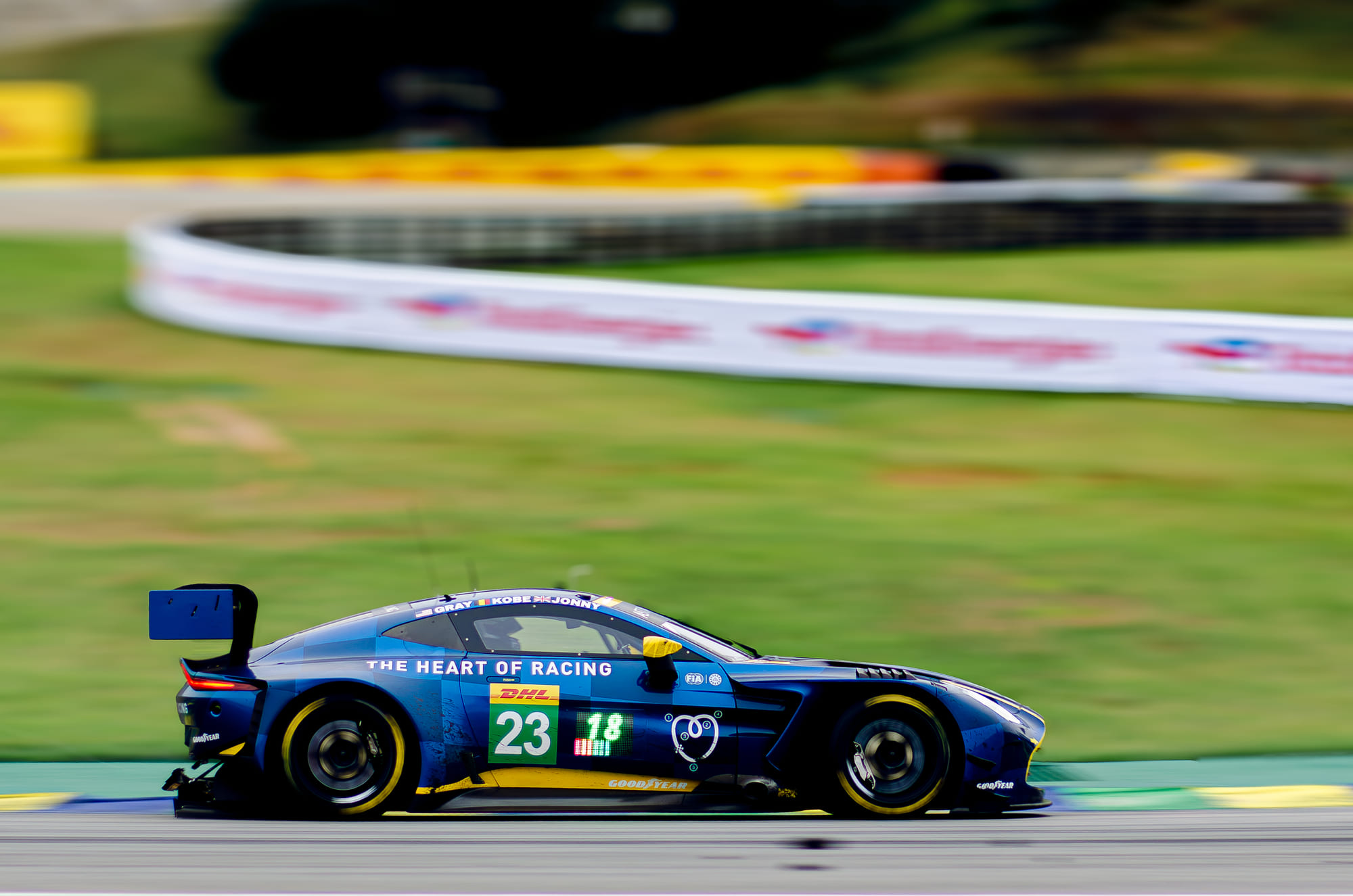 Aston Martin Vantage GT3 #23 da The Heart of Racing, da classe LMGT3, em panning com o gramado varrido ao fundo, pilotado por Gray Newell, Eduardo Barrichello e Jonny Adam no WEC 6 Horas de São Paulo 2026, em Interlagos