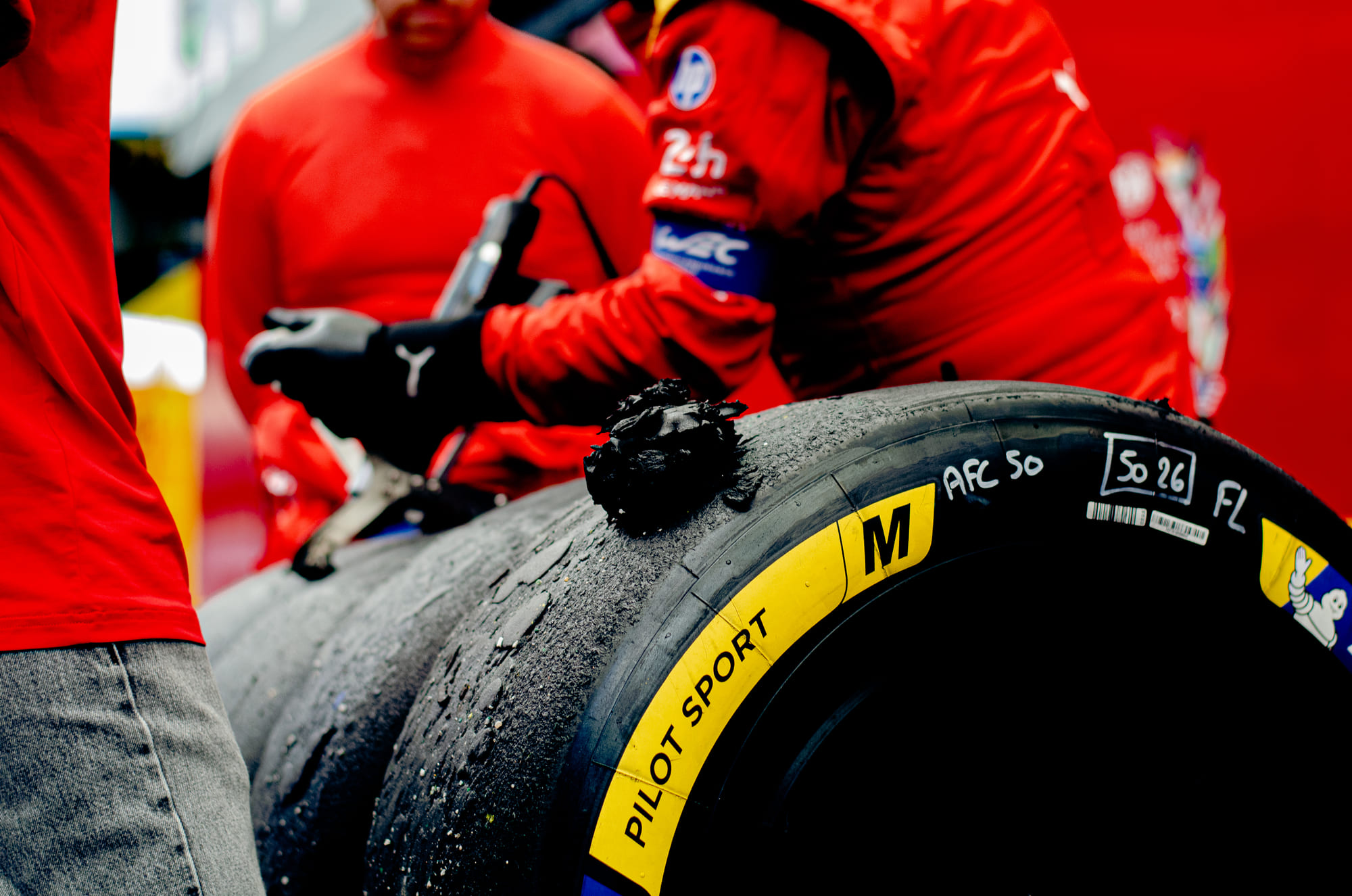 Mecânico da AF Corse com um pneu Michelin usado, marcado à mão "AFC 50" e cheio de borracha grudada, no paddock do WEC 6 Horas de São Paulo 2026, em Interlagos