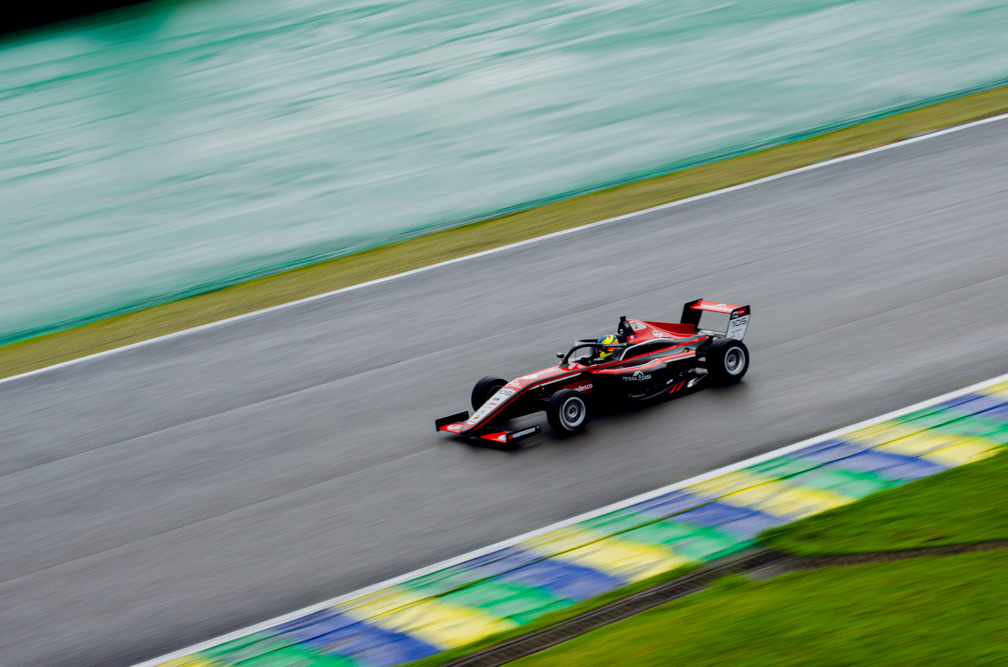 Carro de Fórmula 4 #105 da Cavaleiro Sports, da classe Rookie, em panning com as zebras verde, amarela e azul varridas ao fundo, pilotado por Luiz Queiroz na F4 FIA Brasil 2026 - Etapa 3, Interlagos