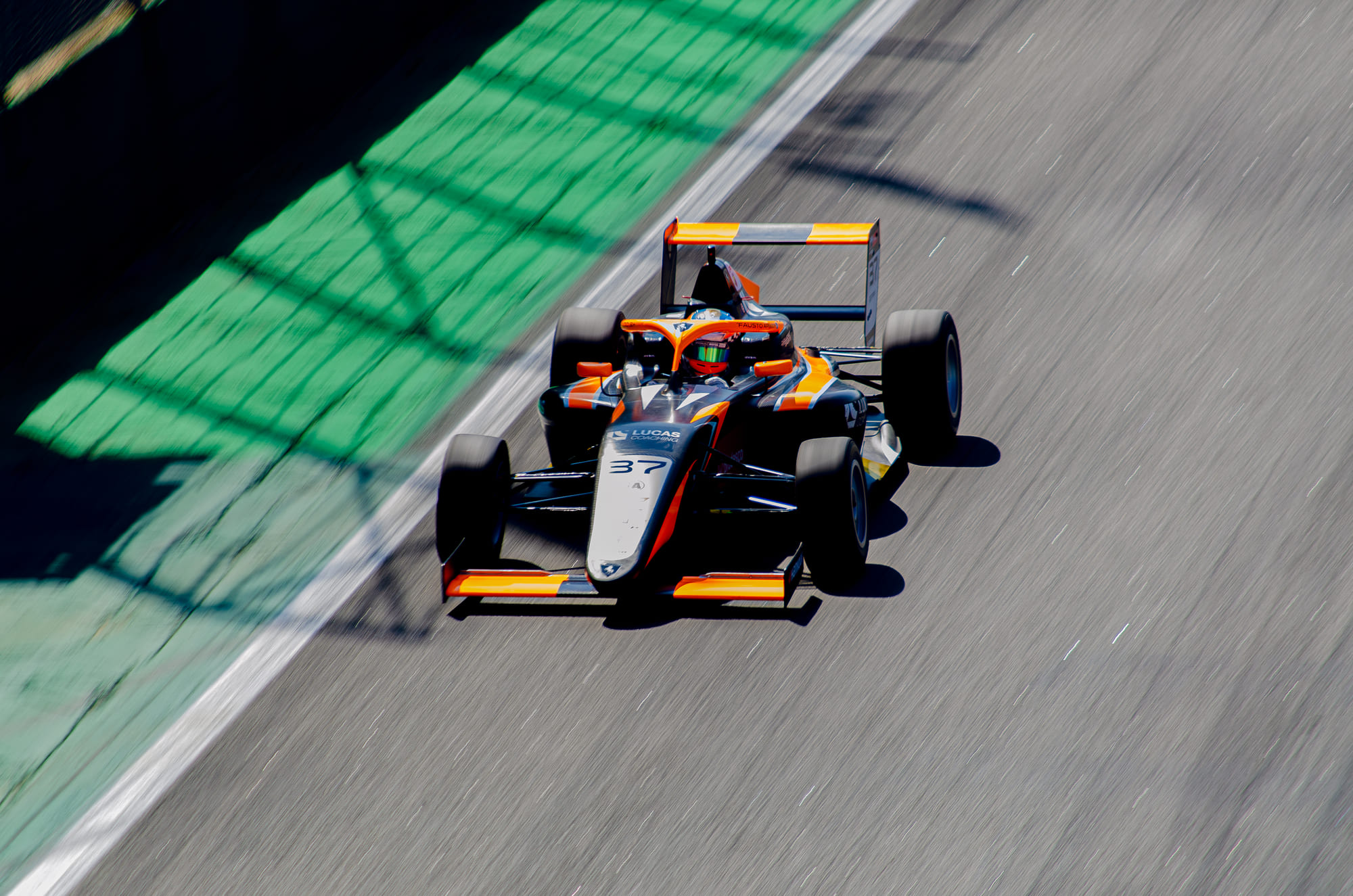 Fórmula 4 #37 da Cavaleiro Sports, da classe Pro, visto de cima cortando a sombra listrada sobre a área verde, com Fausto Arnaudo, na F4 FIA Brasil 2026 - Etapa 3, em Interlagos